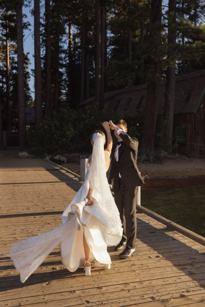 Groom twirls the bride on a wooden dock during their summer wedding portraits