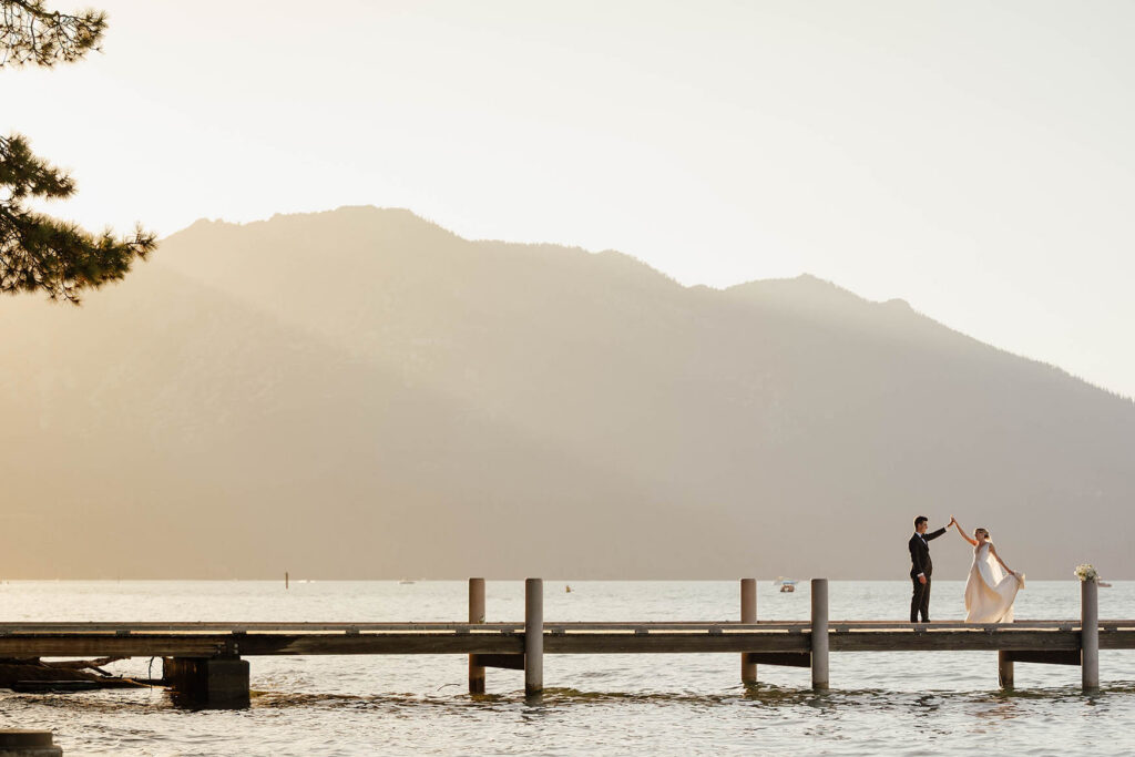 Bride and groom dance on the Lake Tahoe pier with mountains glowing at sunset