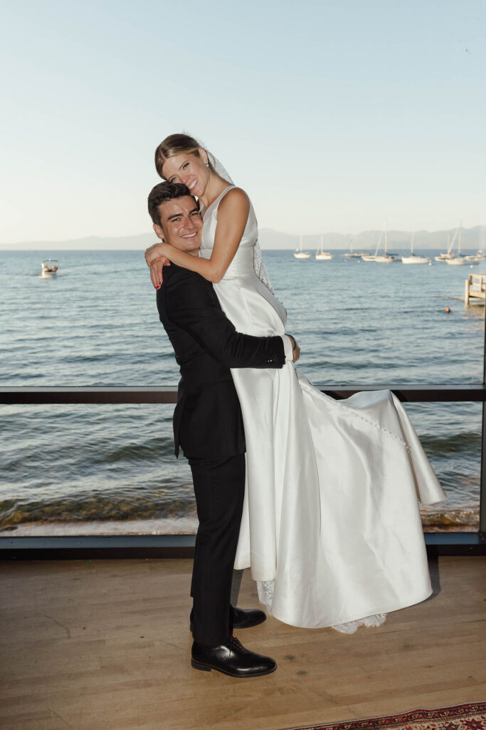 Groom lifts the smiling bride with sailboats and Lake Tahoe behind them
