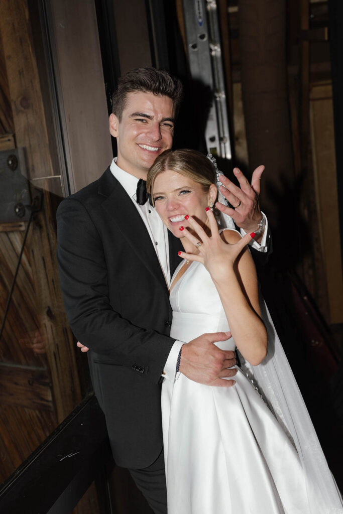 Bride and groom smile and show their wedding rings inside the boathouse