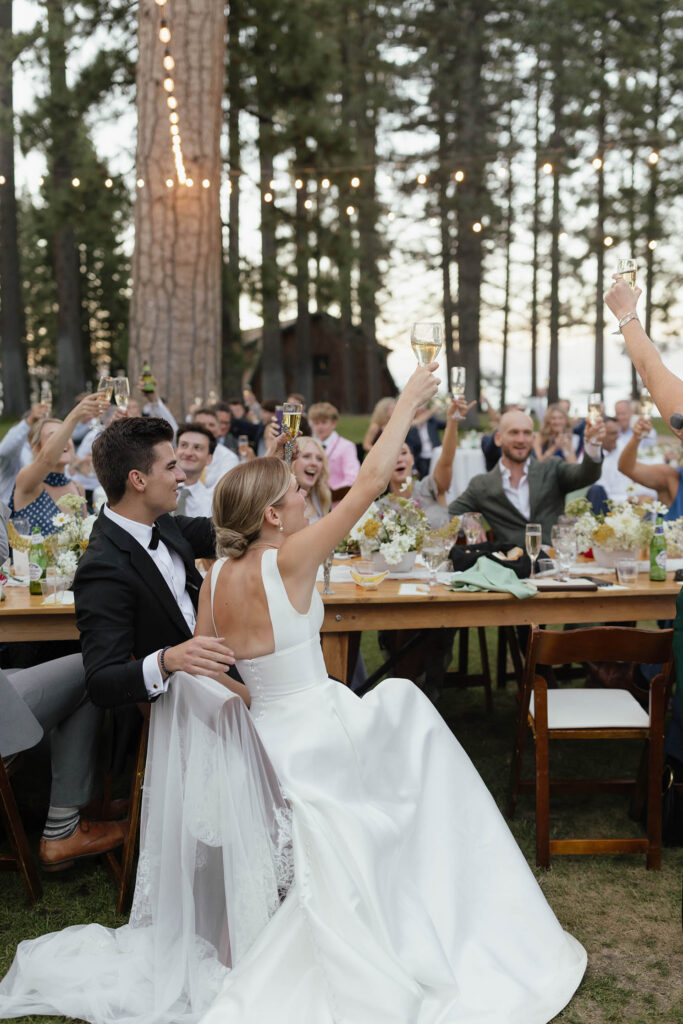 Bride, groom, and guests raise champagne glasses beneath string lights at Valhalla Tahoe