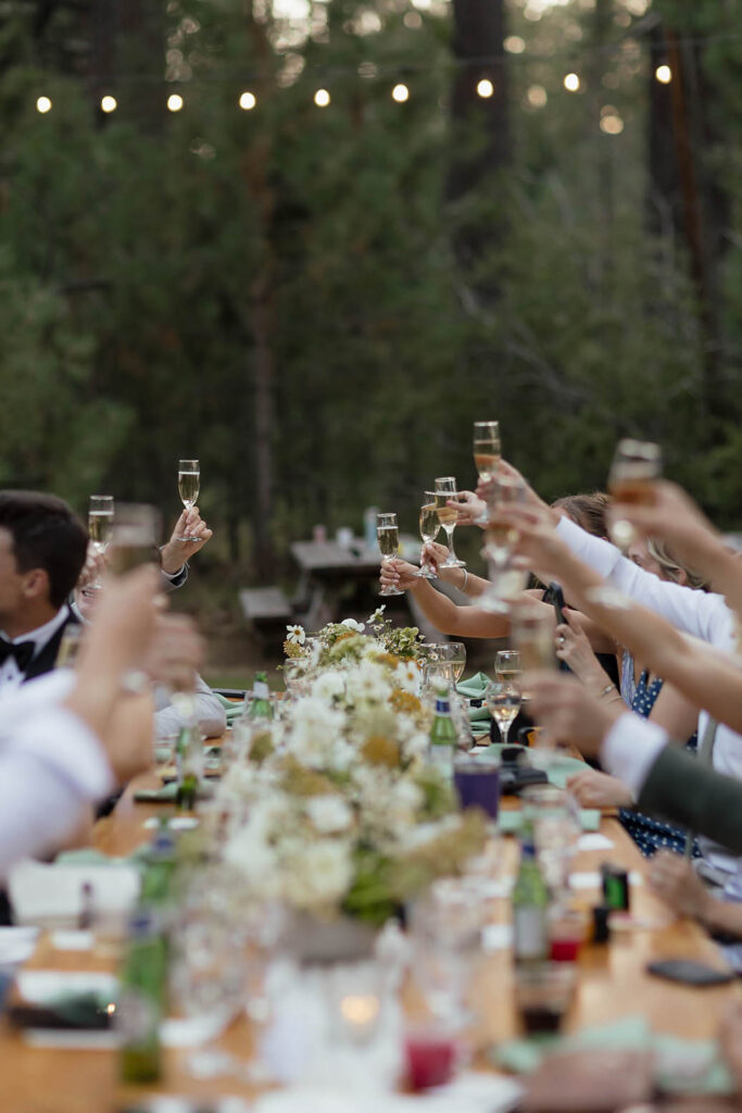 Guests raise champagne glasses beneath string lights during the outdoor summer wedding reception