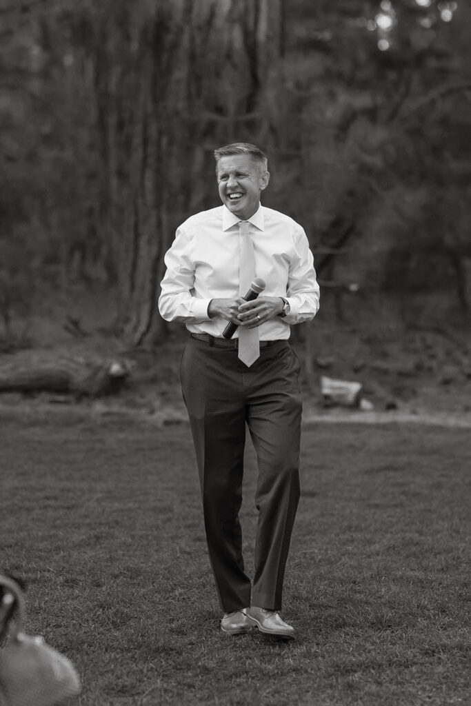 Wedding guest laughs while holding a microphone during an outdoor reception toast
