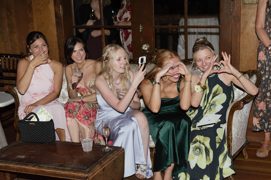 Wedding guests laugh and make heart shapes with their hands during the reception