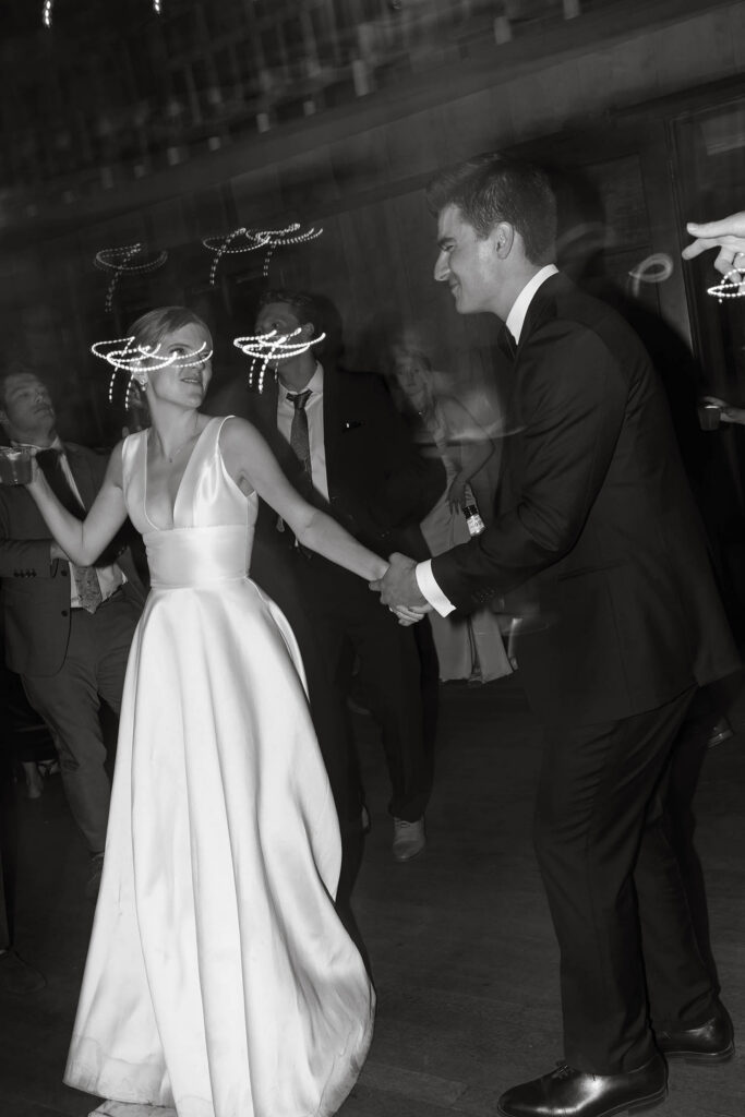 Black-and-white photo of the bride and groom dancing beneath glowing reception lights