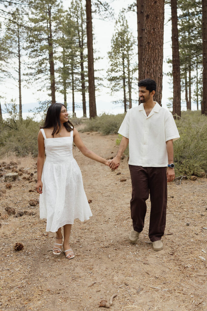 Engaged couple smiling at each other while walking hand in hand through the Lake Tahoe forest