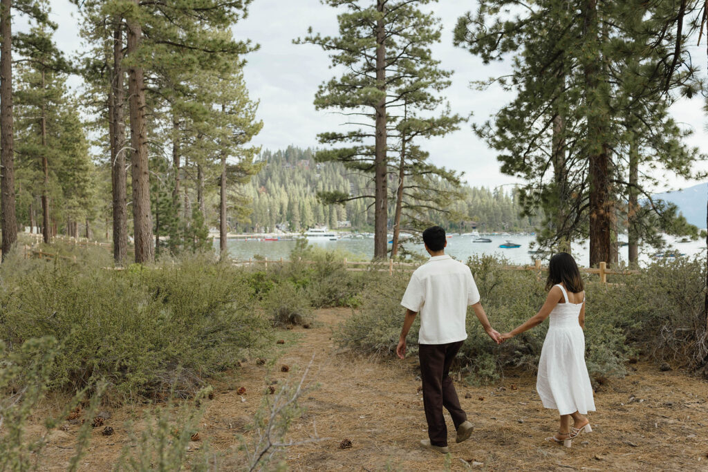 Couple walking toward the Lake Tahoe shoreline surrounded by pine trees and mountain scenery