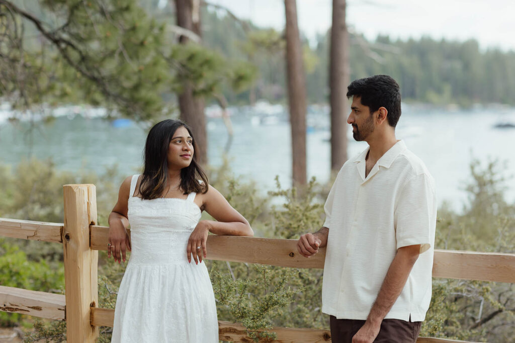 Couple looking at each other while leaning against a wooden fence near Lake Tahoe