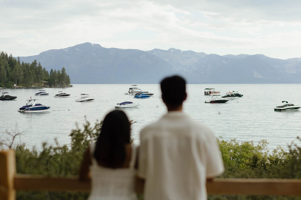 Engaged couple looking across Lake Tahoe toward boats and the surrounding mountains