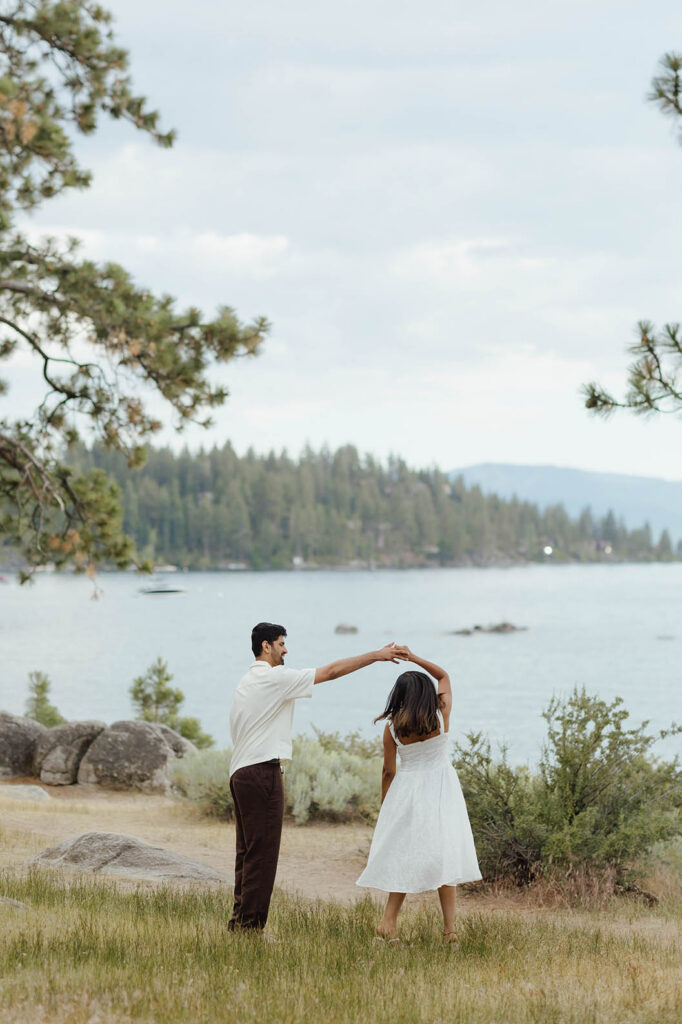 Engaged couple dancing in a grassy meadow overlooking Lake Tahoe
