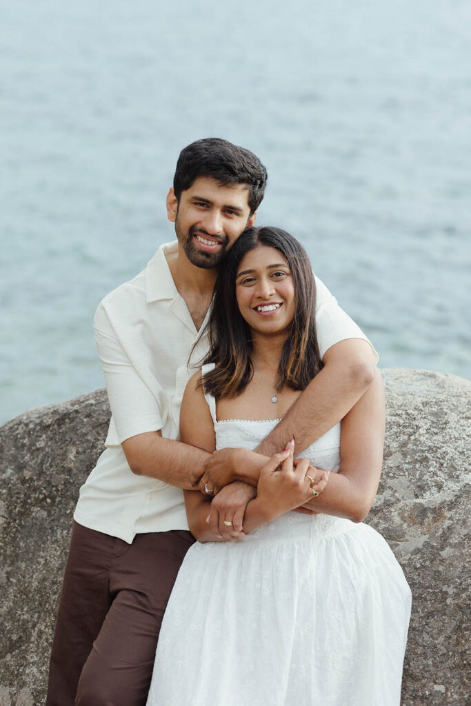 Smiling couple embracing on a boulder beside the calm blue water of Lake Tahoe