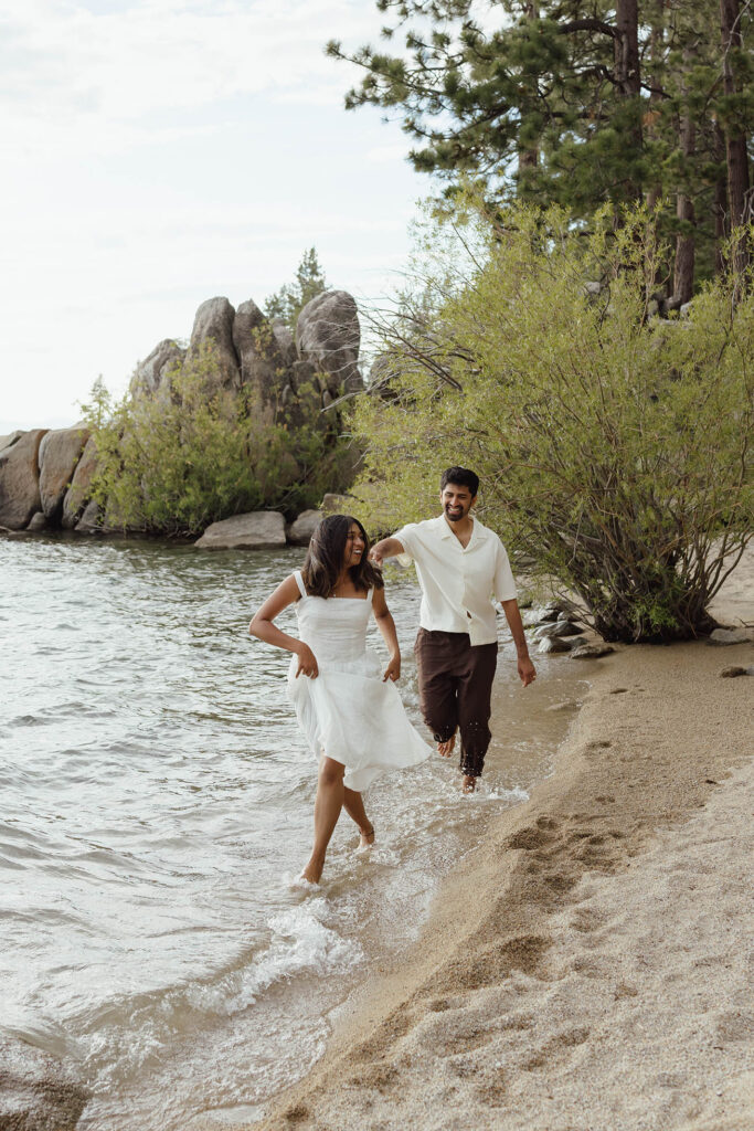 Laughing couple running barefoot through the water during their South Lake Tahoe engagements