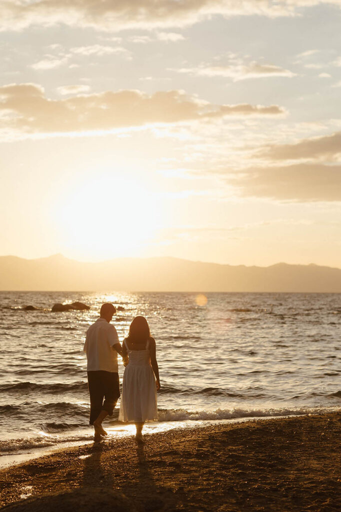 Engaged couple holding hands beside Lake Tahoe during a warm summer sunset