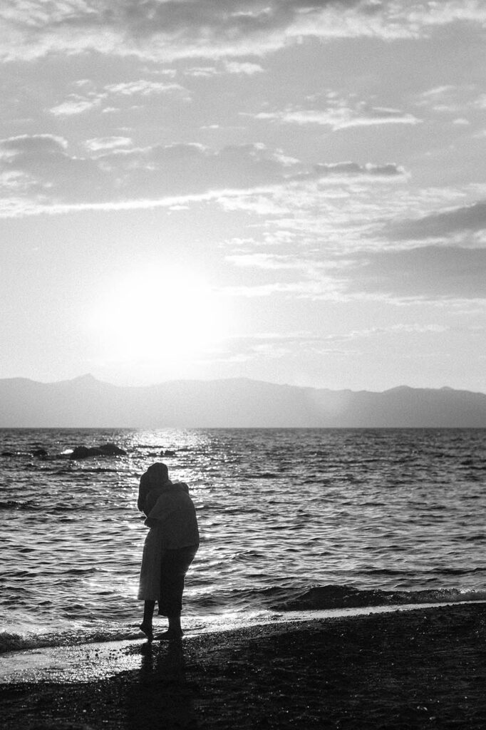 Black-and-white silhouette of an engaged couple embracing along the Lake Tahoe shoreline