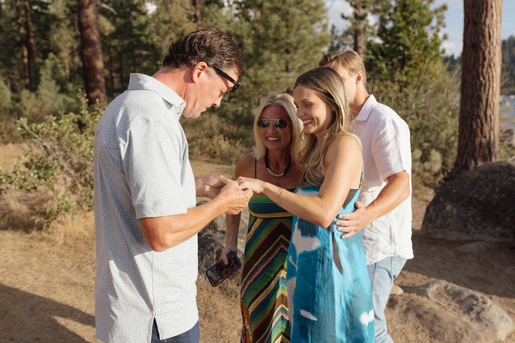 Newly engaged woman showing her ring to family while her fiancé stands behind her with an arm around her waist