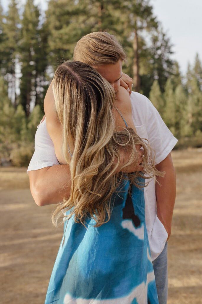 Couple hugging in Lake Tahoe as the man kisses his fiancée’s shoulder and she wraps her arms around his neck