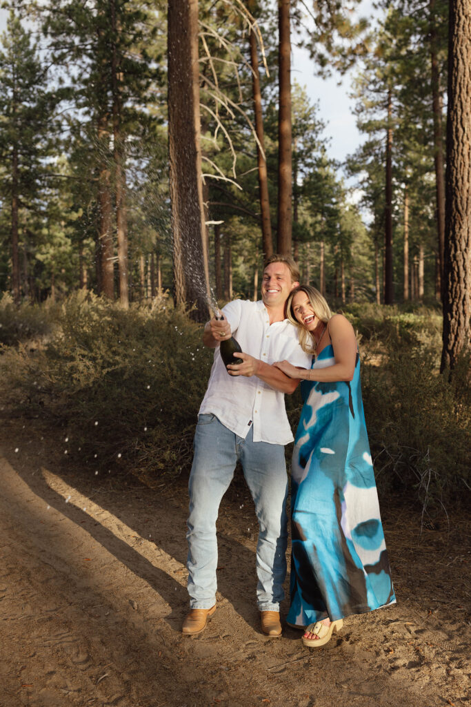 Couple laughing as the man sprays sparkling wine from a bottle during their Lake Tahoe engagement celebration