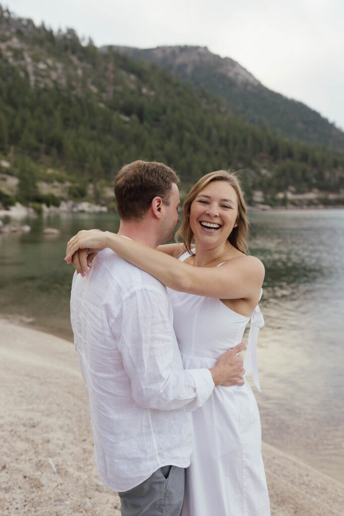 Woman laughing as she embraces her fiancé on the shore during their Lake Tahoe engagement photos