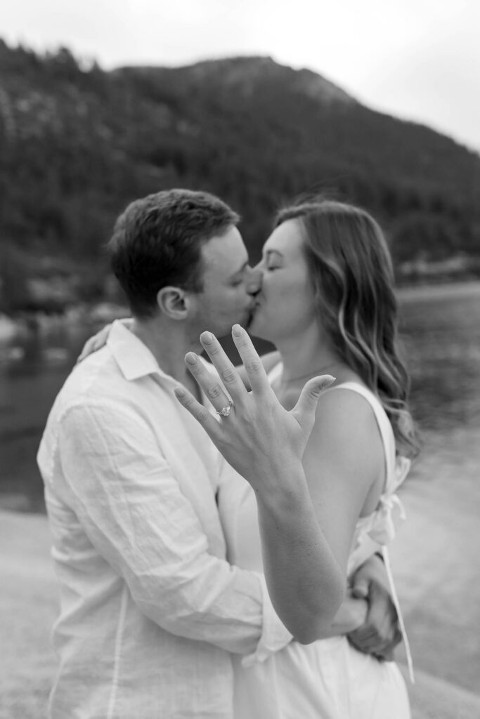 Black-and-white portrait of a couple kissing while the woman shows off her engagement ring