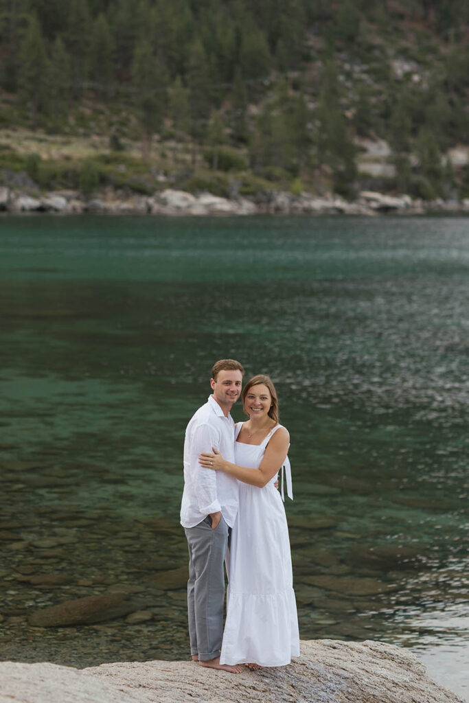 Engaged couple embracing on the shoreline with clear emerald Lake Tahoe water behind them