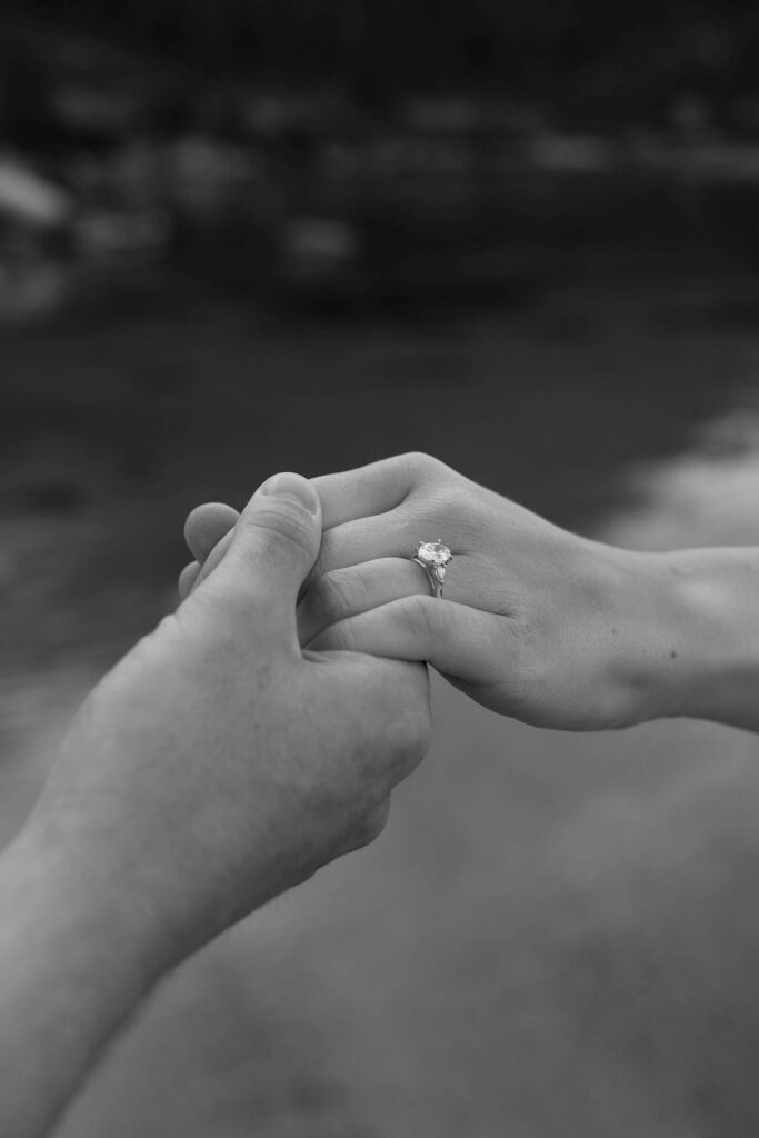 Black-and-white close-up of an engaged couple holding hands and displaying the engagement ring