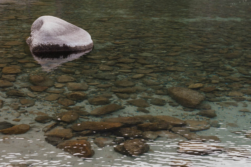 Clear Lake Tahoe water flowing around a sunlit granite rock near the shoreline