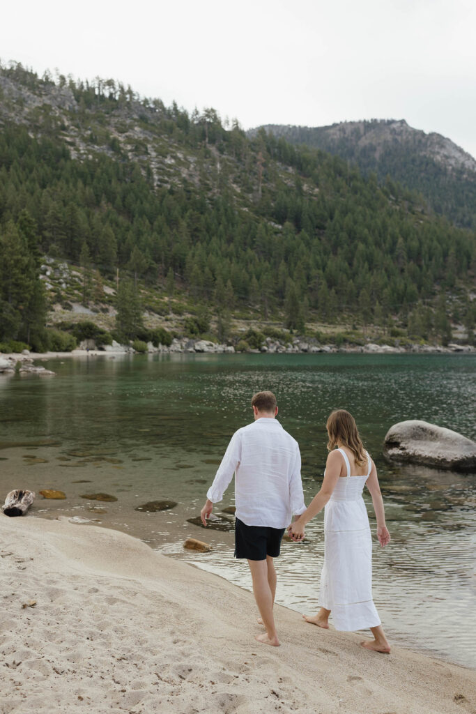 Engaged couple walking hand in hand along a quiet Lake Tahoe beach