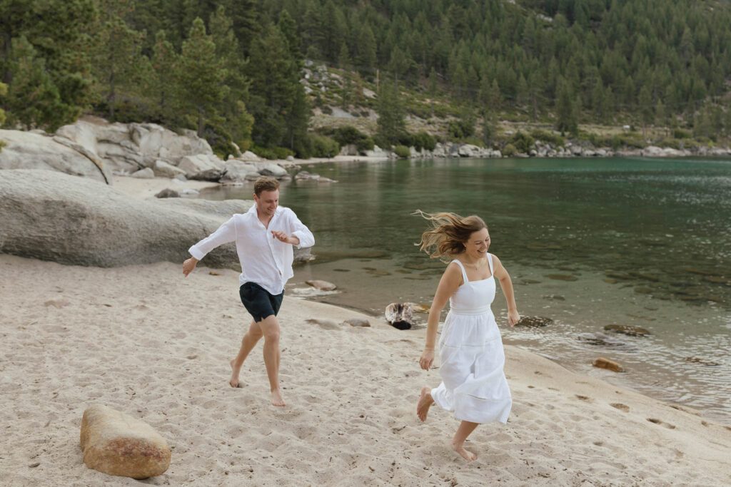 Engaged couple running barefoot along the beach during their in Lake Tahoe at sunrise