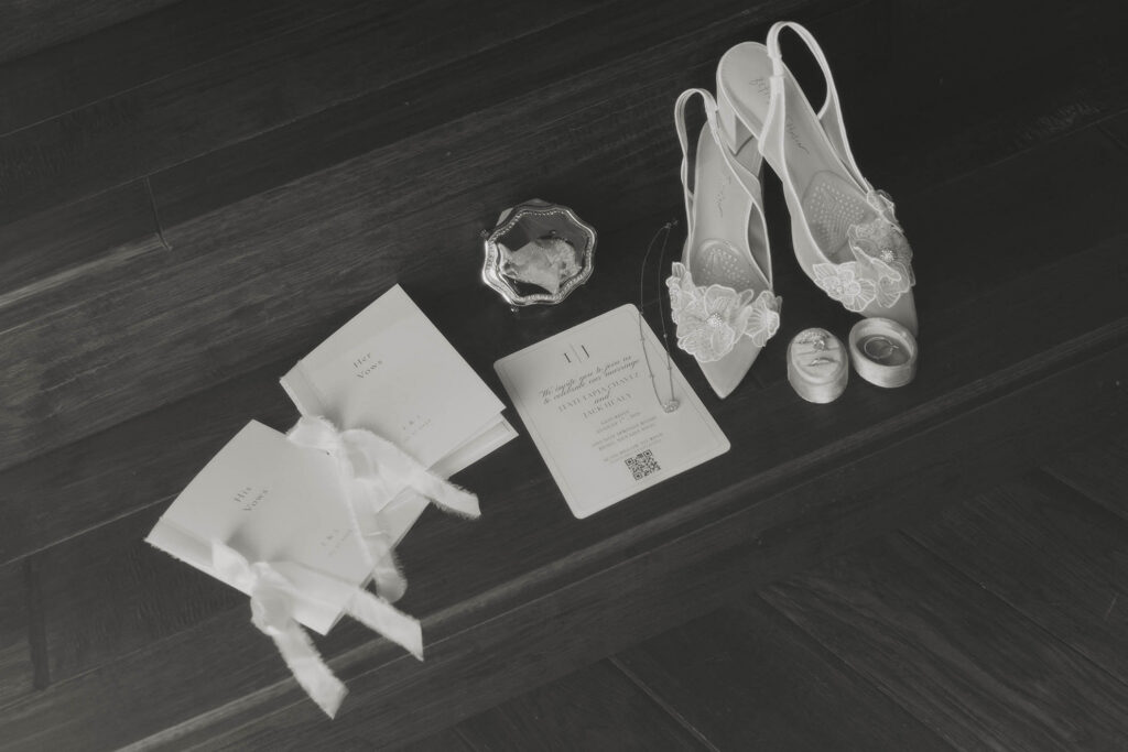 Black-and-white flat lay of bridal heels, vow books, rings and stationery from a Tahoe Blue Estate wedding