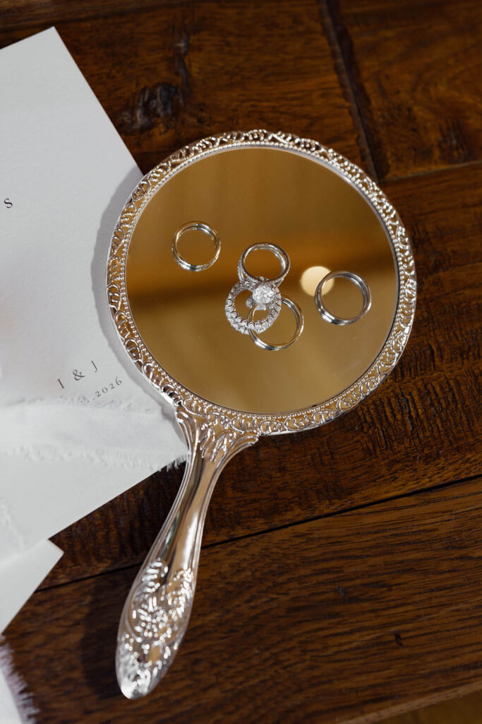 Bride and groom wedding rings arranged on an ornate silver hand mirror beside their vow books