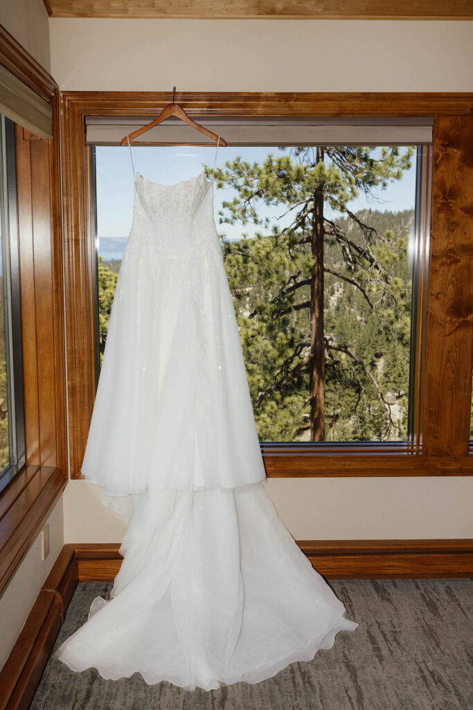 Bride’s lace wedding dress hanging in a window overlooking the forest at Tahoe Blue Estate in Lake Tahoe