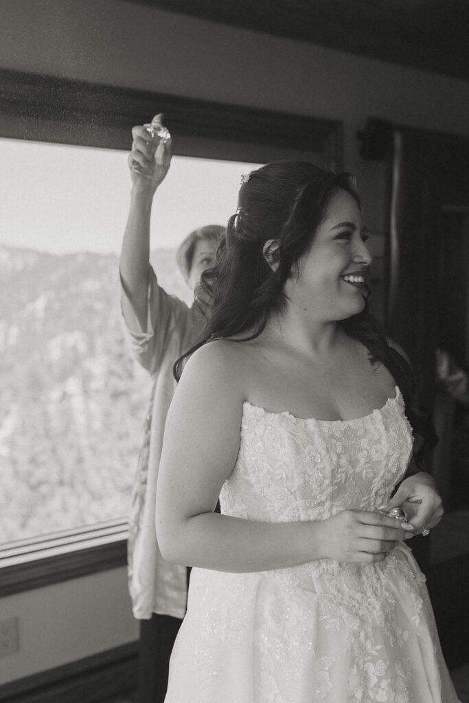 Black-and-white photo of the smiling bride as her hair is finished before the ceremony