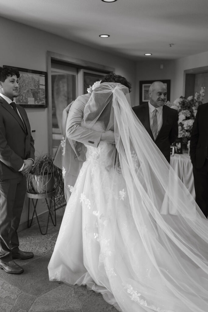 Black-and-white photo of the bride sharing an emotional hug with a loved one beneath her veil