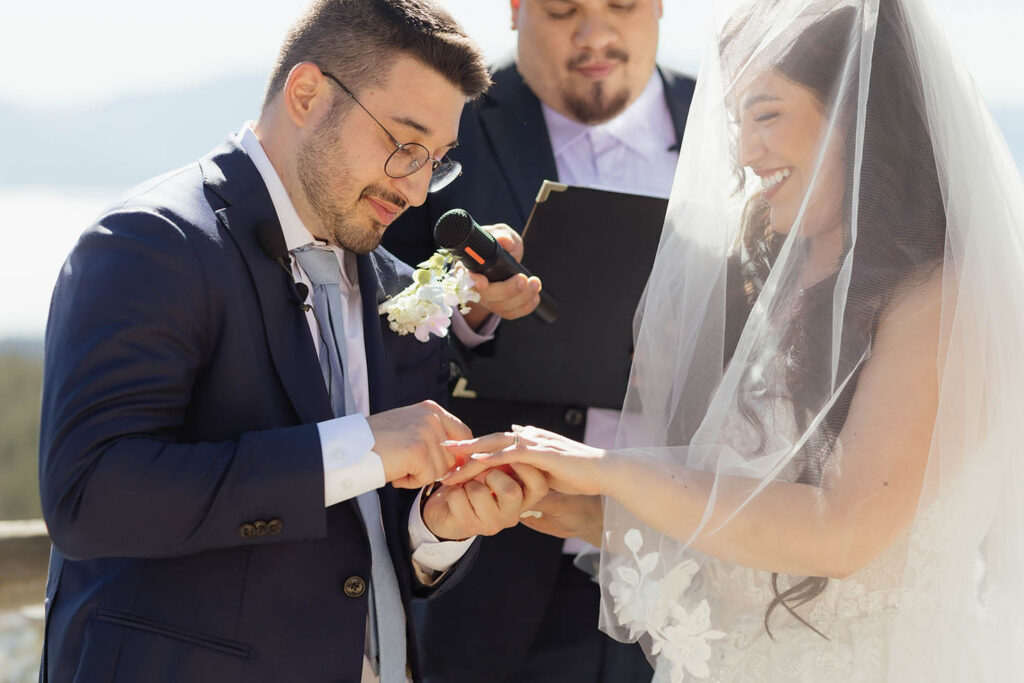 Groom placing a wedding ring on the smiling bride’s finger during their outdoor ceremony