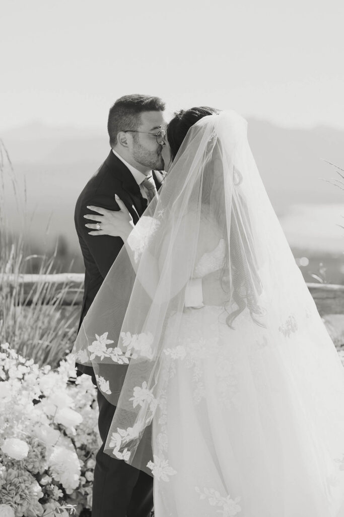 Black-and-white photo of the bride and groom sharing their first kiss beneath her lace veil