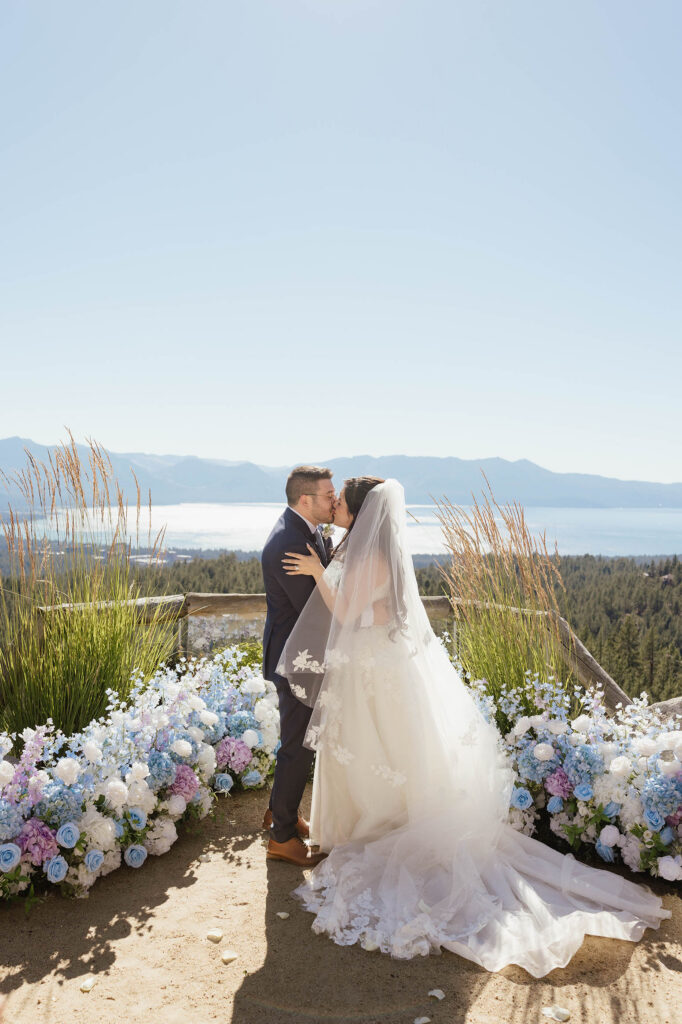 Bride and groom kissing between blue and lavender flowers with Lake Tahoe in the background