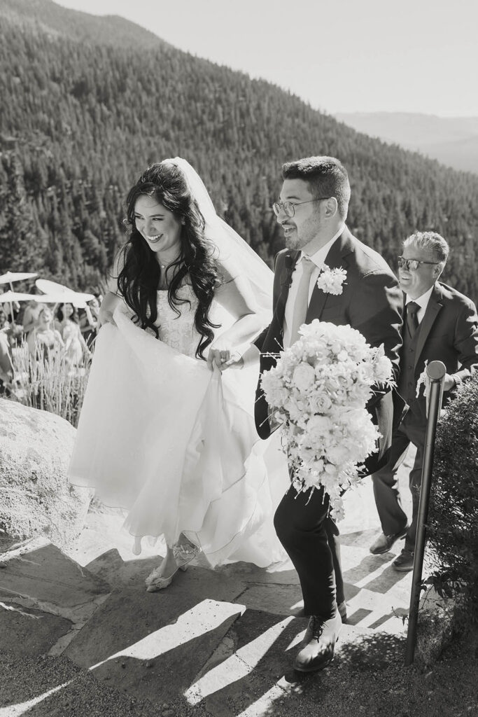 Black-and-white photo of the bride and groom climbing stone steps with her cascading floral bouquet