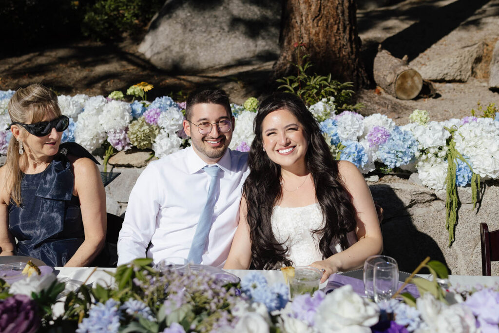 Bride and groom smiling together at their flower-filled outdoor wedding reception