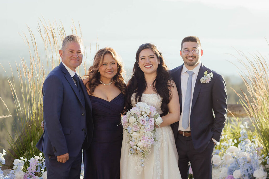 Bride and groom posing with family members beside the outdoor ceremony flowers