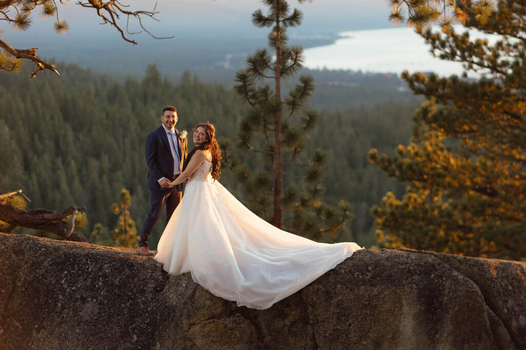Bride and groom holding hands and smiling at sunset with her long wedding dress flowing across the rocks at Tahoe Blue Estate