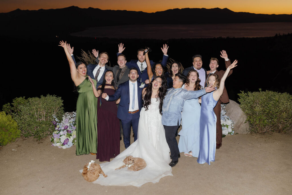 Bride and groom celebrating with wedding guests and two small dogs at sunset