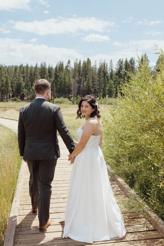 Bride looking back while holding the groom’s hand on a meadow boardwalk in Lake Tahoe