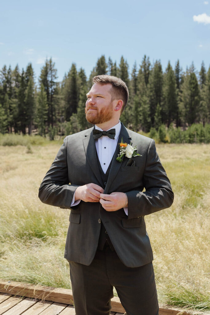 Groom adjusting his dark green suit jacket with a floral boutonniere in a Lake Tahoe meadow