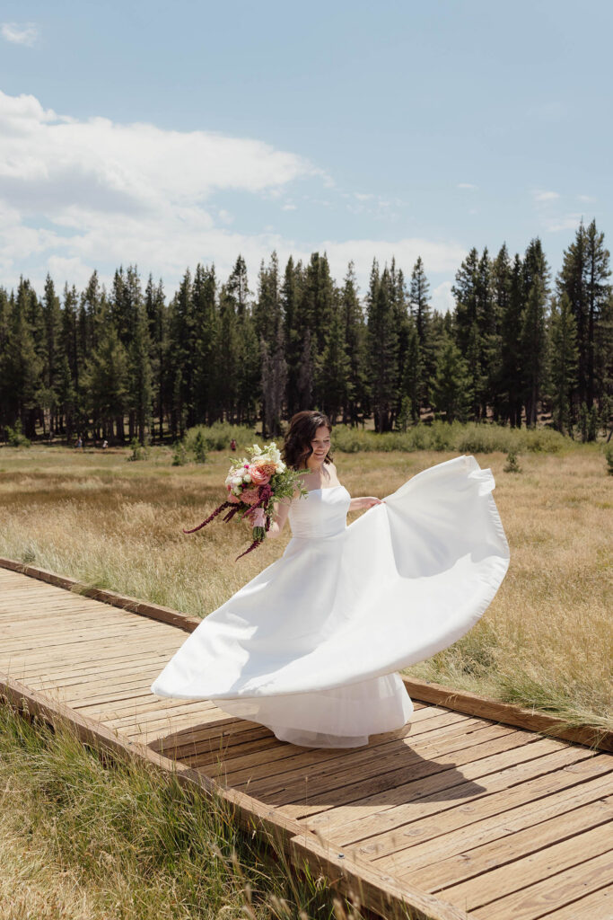 Bride twirling her white wedding dress while holding her bouquet on a meadow boardwalk