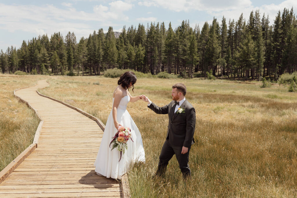 Groom holding the bride’s hand beside a meadow boardwalk during portraits before their Winters Creek Lodge wedding