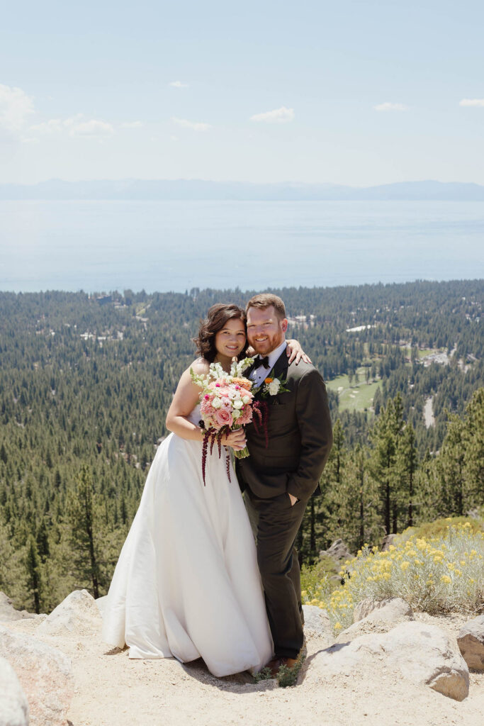 Bride and groom smiling together on a rocky mountainside above Lake Tahoe, with the bride holding a colorful bouquet