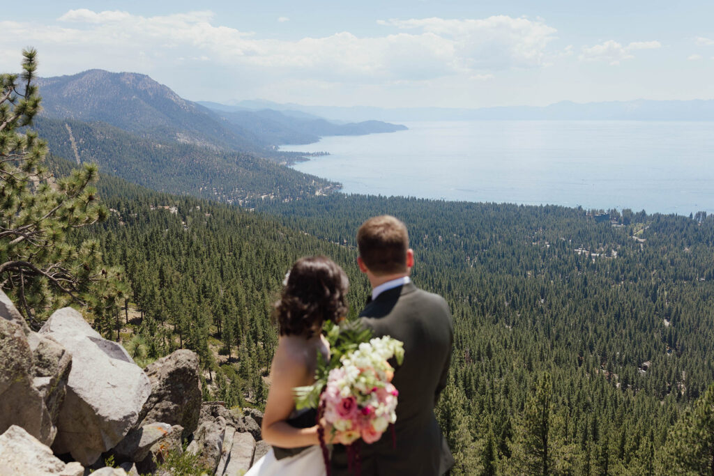 Bride and groom embracing on a rocky overlook with sweeping views of Lake Tahoe and the surrounding pine forest