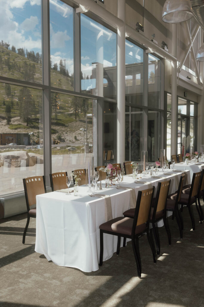 Wedding reception tables with white linens and pink flowers beside floor-to-ceiling windows overlooking the mountains