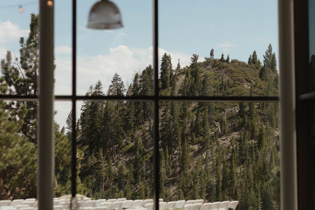 Pine-covered mountains and outdoor ceremony chairs viewed through the tall windows of Winters Creek Lodge near Lake Tahoe