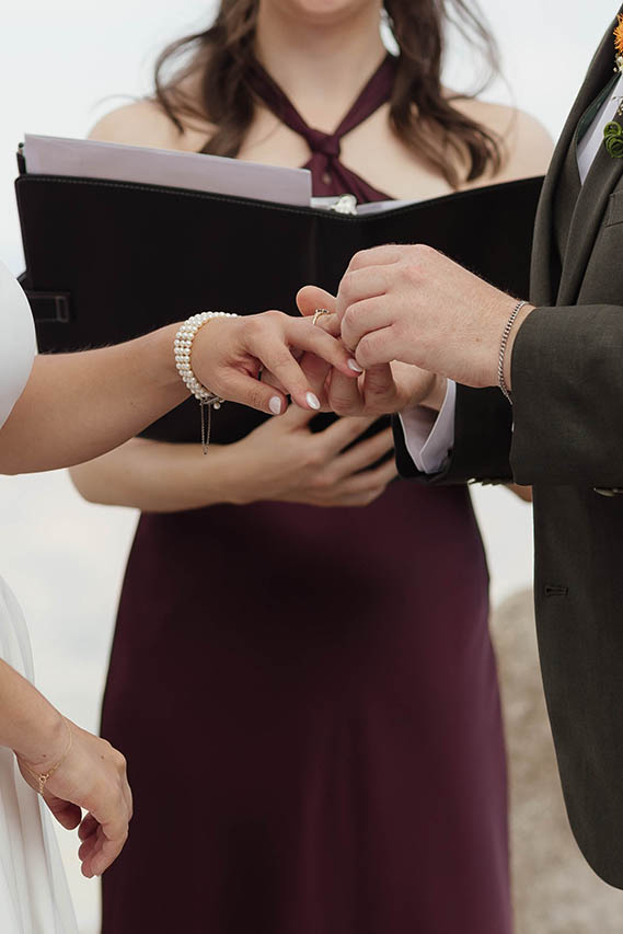 Close-up of the groom sliding a wedding ring onto the bride’s finger during their ceremony